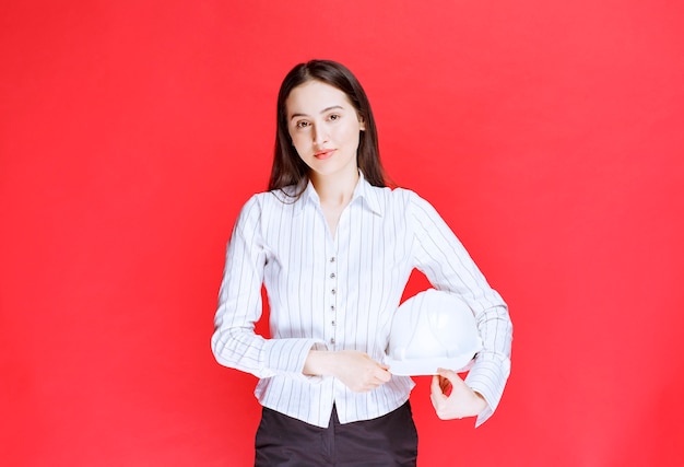 Photo d'une belle femme d'affaires tenant un chapeau de sécurité sur un mur rouge.