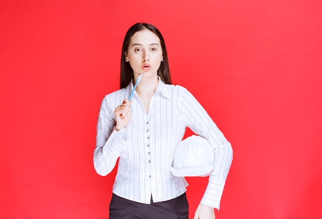 Photo d'une belle femme d'affaires tenant un chapeau de sécurité sur un mur rouge.