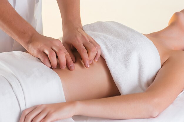 La photo de la belle femme dans le salon de massage et les mains des hommes sur son corps