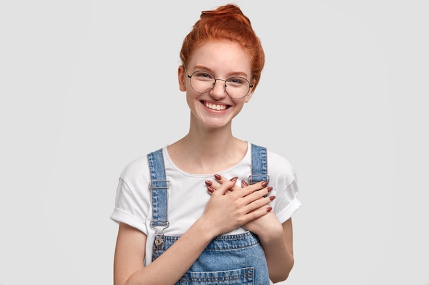 Photo de belle femme positive garde les deux mains sur le cœur, a un sourire agréable, exprime sa gratitude