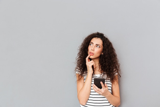 Photo gratuite photo d'une belle femme touchant ses lèvres et regardant de côté tout en pensant à quelque chose d'important ou en essayant de se souvenir par-dessus un mur gris