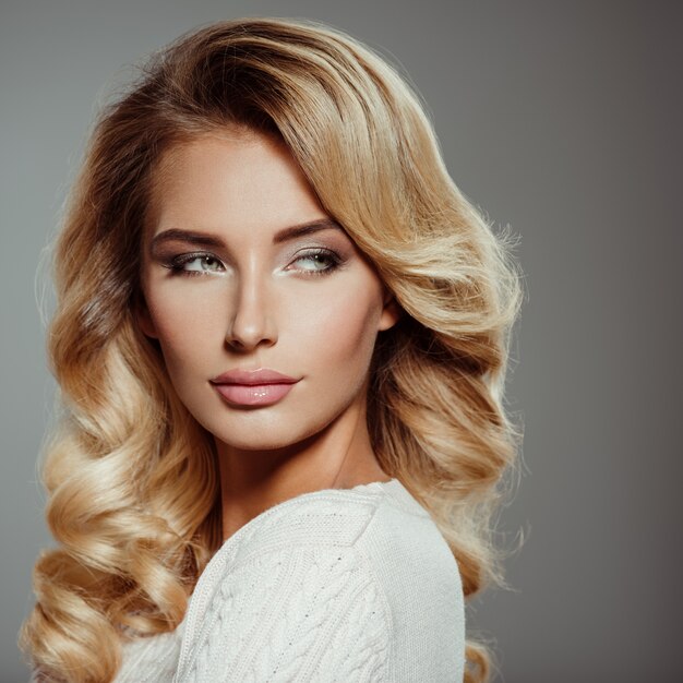 Photo d'une belle jeune femme blonde aux cheveux bouclés. Gros plan visage sensuel attrayant de femme blanche. Maquillage pour les yeux Smokey.