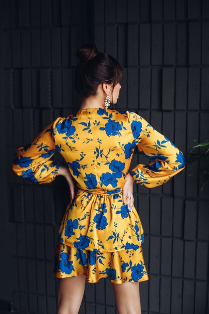 Photo d'une belle jeune femme caucasienne aux cheveux noirs en robe jaune et bleue, des chaussures dorées montrent différentes poses pour l'appareil photo