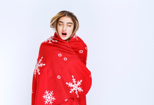 Photo d'une belle jeune femme enveloppée dans une couverture douce contre un mur blanc.