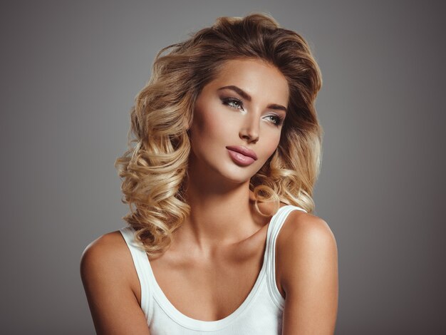 Photo d'une belle jeune fille blonde aux cheveux bouclés. Gros plan visage sensuel attrayant de femme blanche aux cheveux longs. Maquillage pour les yeux Smokey.