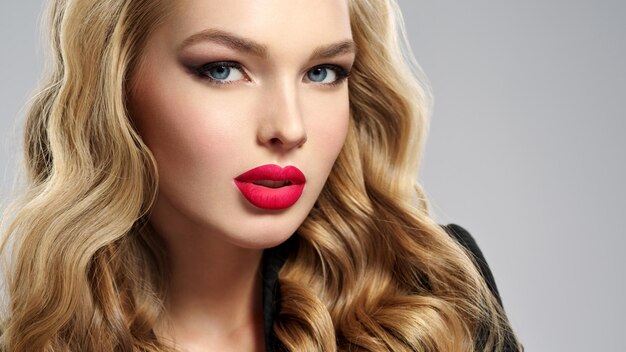 Photo d'une belle jeune fille blonde aux lèvres rouges sexy. Gros plan visage sensuel attrayant de femme blanche aux cheveux longs. Maquillage pour les yeux fumés