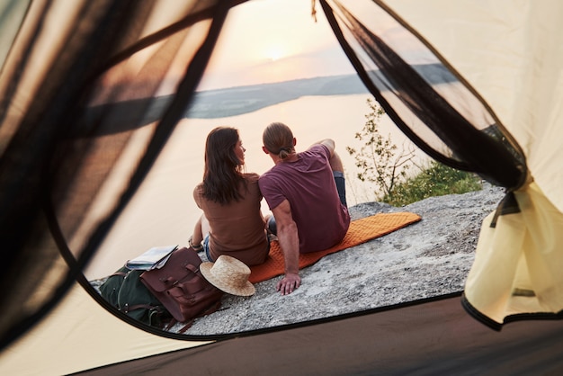 Photo d'un couple heureux assis dans une tente avec vue sur le lac lors d'une randonnée.