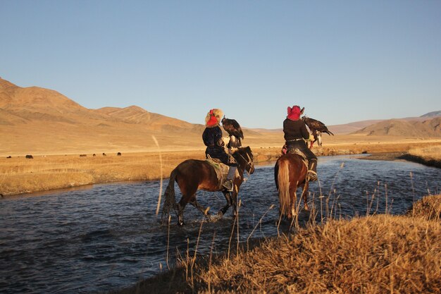 Photo de deux cavaliers dans une rivière entourée d'une vallée déserte avec des collines