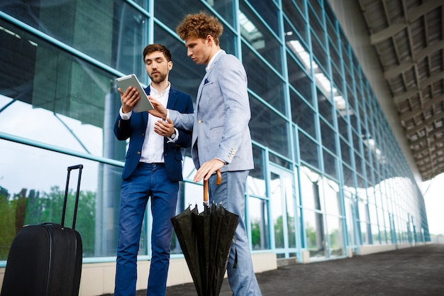 Photo de deux jeunes hommes d'affaires parlant à l'aéroport et tenant la tablette