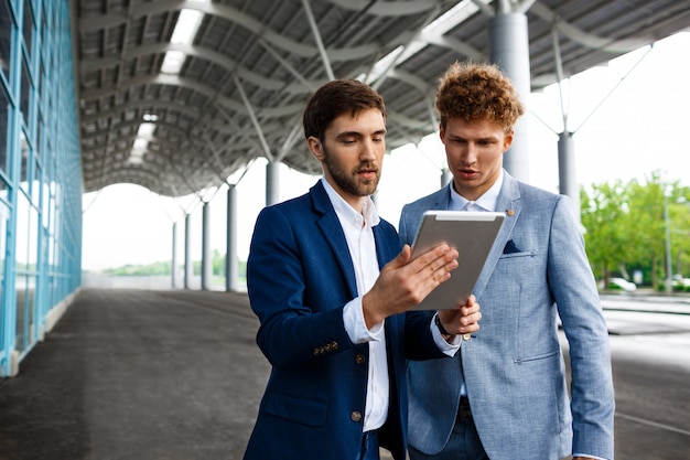 Photo de deux jeunes hommes d'affaires parlant sur la station et tenant la tablette