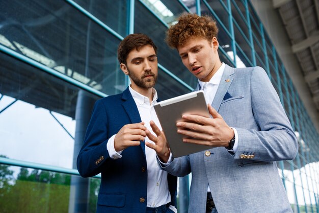 Photo de deux jeunes hommes d'affaires parlant sur la station et tenant la tablette