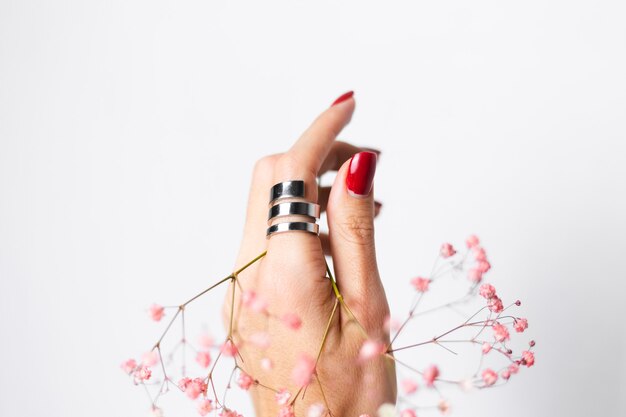 Photo douce et douce de la main de la femme avec manucure rouge grand anneau tenir de jolies petites fleurs séchées roses sur blanc.