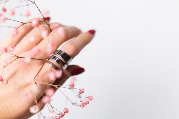 Photo douce et douce de la main de la femme avec manucure rouge grand anneau tenir de jolies petites fleurs séchées roses sur blanc.