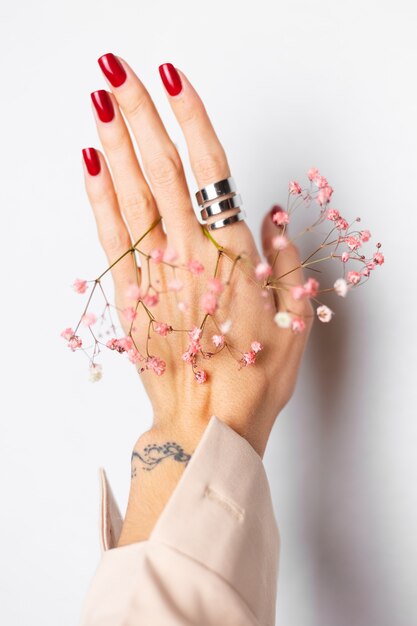 Photo douce et douce de la main de la femme avec manucure rouge grand anneau tenir de jolies petites fleurs séchées roses sur blanc.