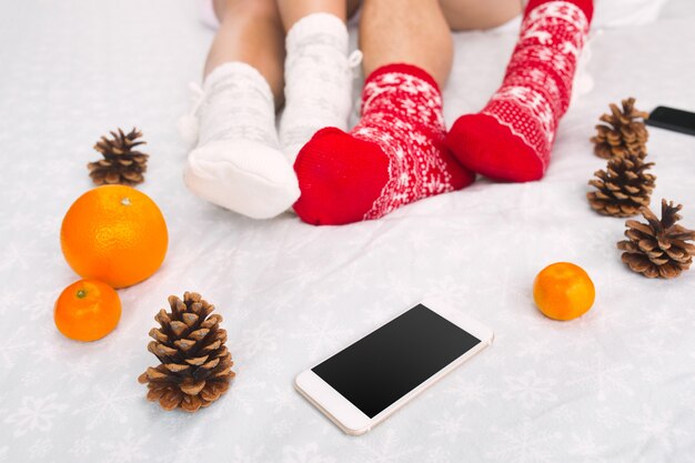 Photo douce de femme et homme sur le lit avec téléphone et fruits, point de vue de dessus. Jambes féminines et masculines du couple dans des chaussettes de laine chaudes.