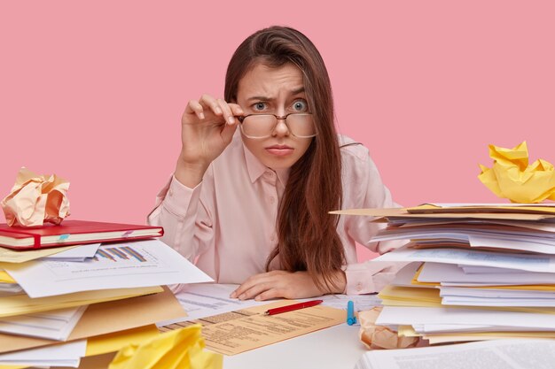 Photo de drôle de femme regarde à travers d'épaisses lentilles de lunettes, a surpris l'expression indignée, beaucoup de paperasse