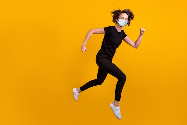 Photo du corps pleine longueur d'une fille sautant en cours d'exécution dans un centre commercial utiliser un masque médical isolé sur fond de couleur jaune