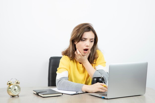 Photo d'une employée de bureau assise au bureau avec un ordinateur portable et un presse-papiers. Photo de haute qualité