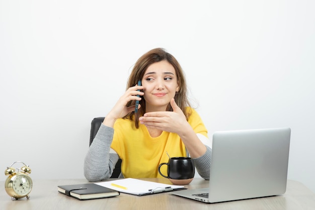 Photo d'une employée de bureau assise au bureau et parlant sur un téléphone portable. Photo de haute qualité