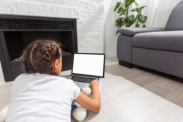 Photo d'une enfant positive qui étudie un ordinateur portable à distance avec une leçon de communication en ligne avec un tuteur écrit un rapport dans la maison à l'intérieur