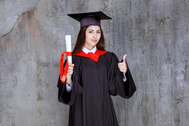 Photo d'une étudiante avec un certificat de fin d'études qui lève le pouce. Photo de haute qualité