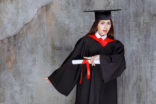 Photo d'une étudiante portant une toge pointant vers quelque part. Photo de haute qualité