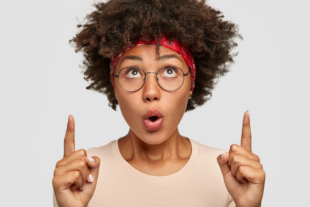 La photo d'une femme afro surprise indique avec les deux index, garde la bouche largement ouverte