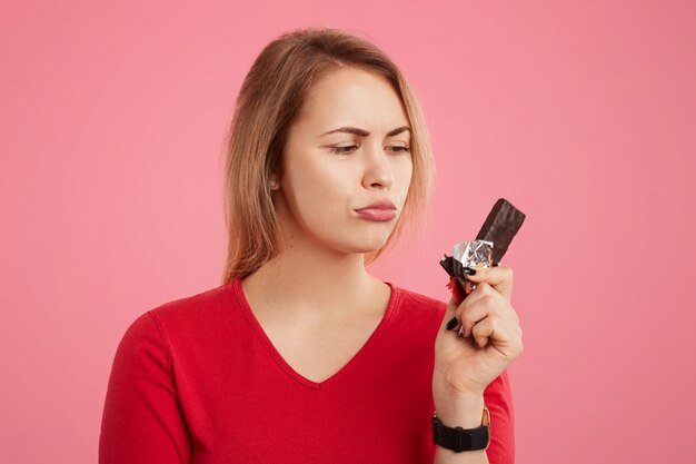 Photo d'une femme avec une barre de chocolat sucrée, suit un régime, veut manger quelque chose de sucré