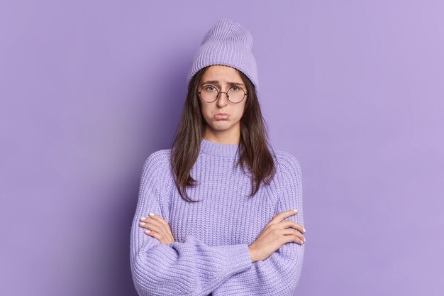 Photo de femme brune mécontente regarde avec une expression offensée garde les mains croisées étant blessé par quelqu'un porte des lunettes rondes vêtements violets. La femelle grincheuse est de mauvaise humeur. Concept de ressentiment