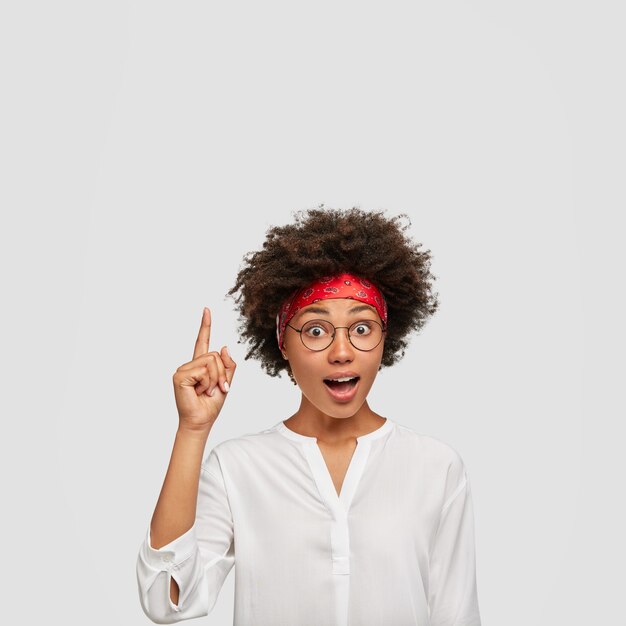 Photo d'une femme ethnique surprise avec une expression stupéfaite, pointe l'index vers le haut, obtient une idée intéressante