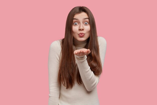 Photo d'une femme européenne heureuse fait un baiser aérien à distance, flirte avec quelqu'un, a une expression heureuse