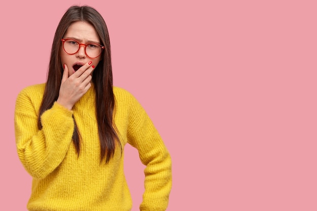 Photo d'une femme fatiguée brune mécontente bâille et couvre la bouche avec palm