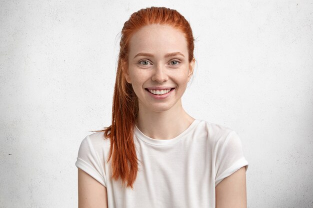 Photo d'une femme gingembre assez satisfaite, a les yeux verts, la peau tachetée de rousseur, sourit agréablement, étant de bonne humeur alors qu'elle passe du temps libre en cercle familial