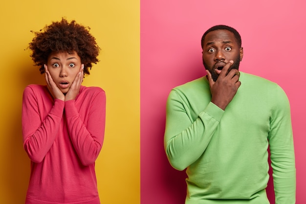 Photo gratuite photo d'une femme et d'un homme ethniques émus, terrifiés par des nouvelles choquantes, n'en croient pas leurs yeux, posent contre un mur rose et jaune vif. concept de personnes et d'émotions