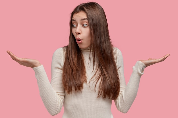 Photo D'une Femme Indécise écarte Les Mains, A Une Expression Désemparée, Des Doutes Entre Deux Articles, Porte Une Tenue Décontractée