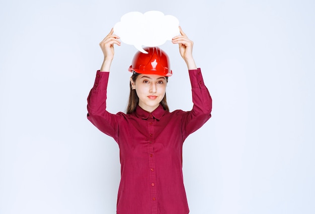 Photo d'une femme ingénieur en casque rouge tenant une bulle de dialogue vide sur fond blanc.