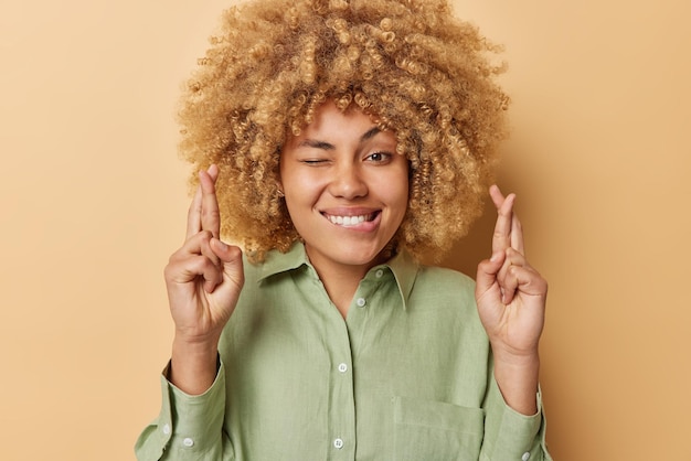 Photo gratuite photo d'une femme pleine d'espoir se mord les lèvres garde les doigts croisés croit en la bonne chance fait un vœu chéri prie pour un miracle espère que de bonnes choses se produiront porte une chemise en lin vert isolée sur un mur beige