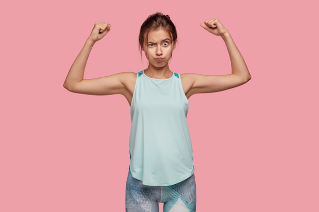 Photo d'une femme sportive en bonne santé montre les biceps et les muscles, lève les mains