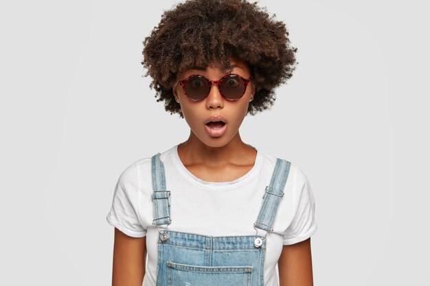 Photo d'une femme surprise à la peau foncée avec une coiffure afro, garde la bouche ouverte, réagit à de fausses nouvelles soudaines