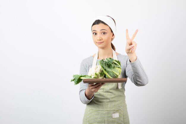 Photo d'une femme en tablier avec une assiette en bois de choux-fleurs montrant le signe de la victoire