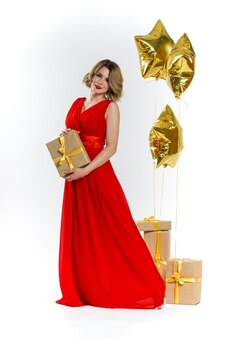 Photo de fête d'élégance dame sexy en robe rouge avec des lèvres rouges et de beaux cheveux blonds bouclés, souriant. contexte des ballons à air doré et des cadeaux. concept de la vente