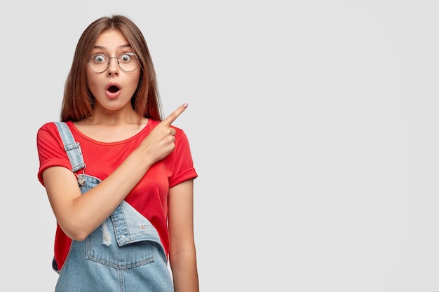 Photo gratuite photo d'une fille aux cheveux noirs stupéfaite avec haleine, regarde avec des yeux buggés, choquée par les prix élevés