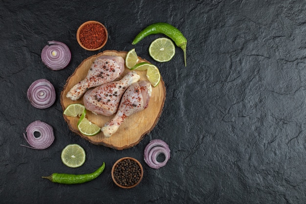 Photo grand angle de pilons de poulet cru et légumes sur planche de bois.