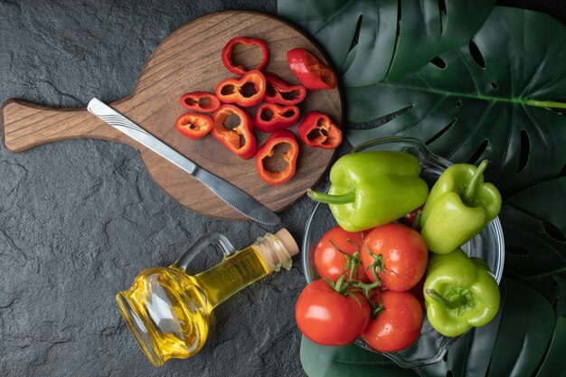 Photo grand angle de tomates mûres avec du poivre dans un bol et du poivron rouge tranché sur une planche de bois.