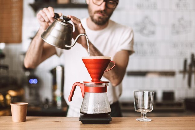 La photo en gros plan d'un barista debout au comptoir et préparant le versement d'un café au café