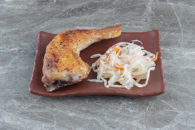 La photo en gros plan d'une cuisse de poulet grillée avec de la choucroute sur une plaque en céramique brune.