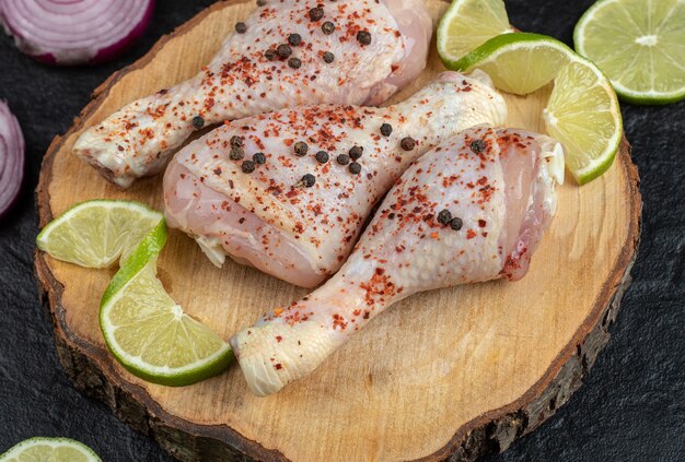 La photo en gros plan de cuisses de poulet crues épicées avec de la chaux sur planche de bois.