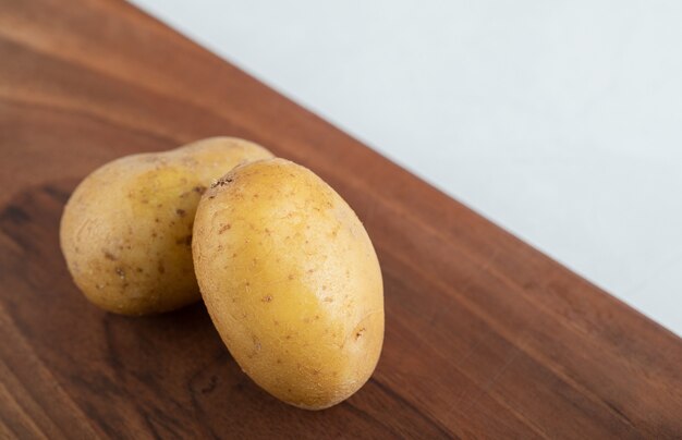 La photo en gros plan de deux pommes de terre fraîches sur planche de bois brun