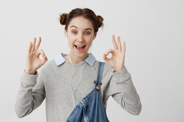 Photo gros plan d'une femme séduisante montrant bien avec les doigts, profitant de la musique des écouteurs. Femelle adulte de bonne humeur après avoir écouté un livre audio avec son smartphone. Le langage du corps