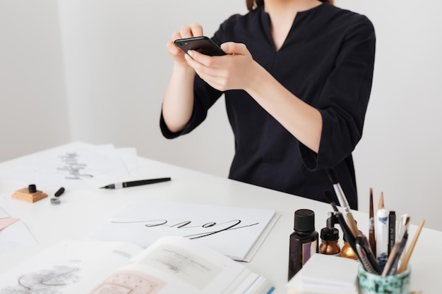 Photo en gros plan d'une fille assise au bureau blanc et prenant des photos de notes sur son téléphone portable isolé